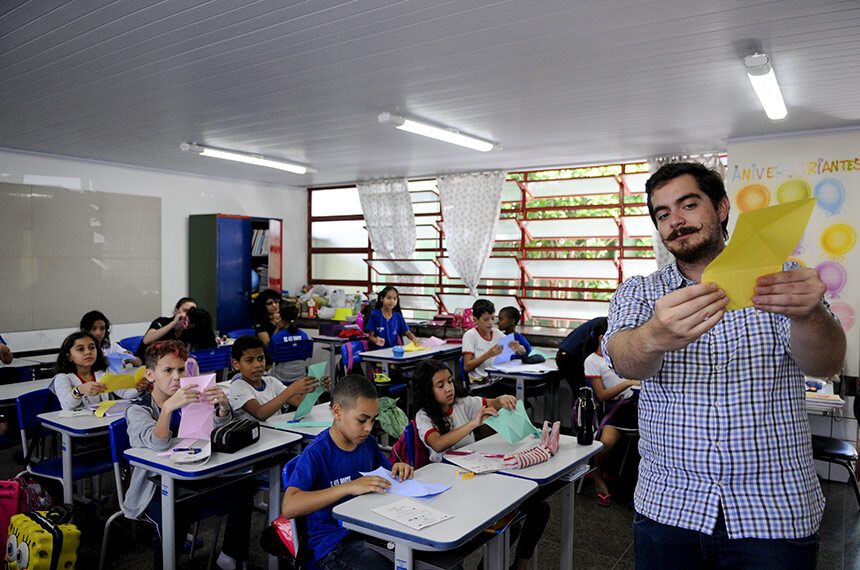 Professor mostra uma dobradura de papel a alunos do ensino fundamental em uma sala de aula