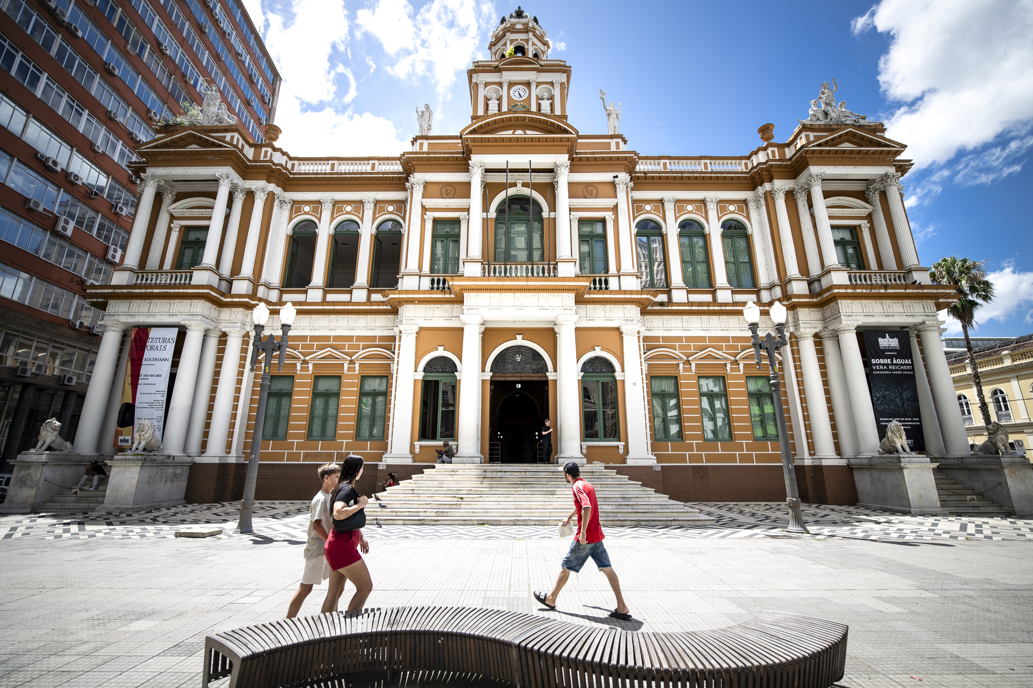 Fachada do Paço Municipal de Porto Alegre em dia de sol, com pedestres passando em frente ao prédio